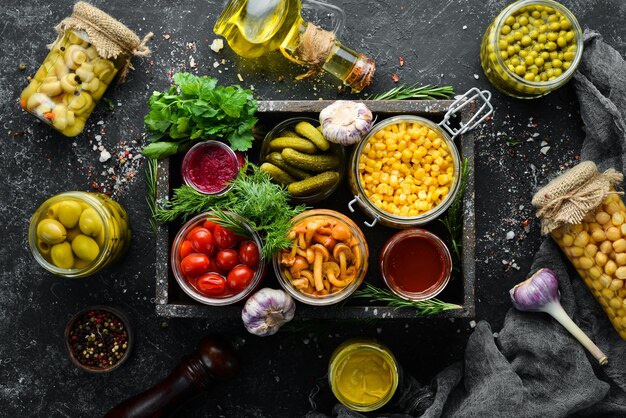 Légumes et champignons marinés dans des bocaux en verre dans une boîte en bois sur fond de pierre noire Vue de dessus