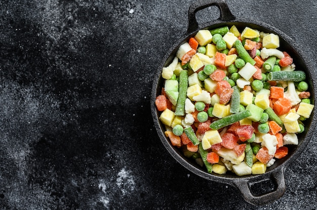 Légumes crus surgelés dans une casserole. Végétarisme. Fond noir.