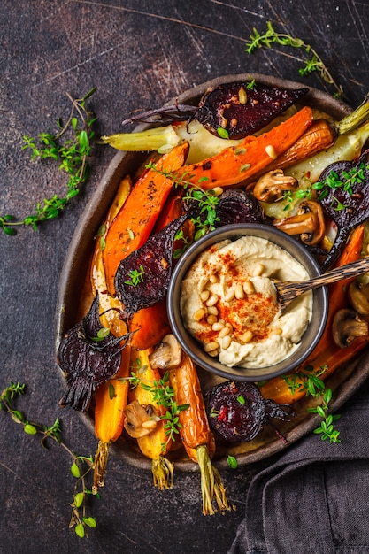 Légumes cuits au four avec du houmous dans un plat sombre, vue de dessus.