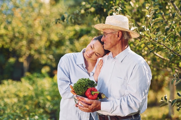 Avec des légumes dans les mains, la fille est avec son père aîné dans le jardin pendant la journée