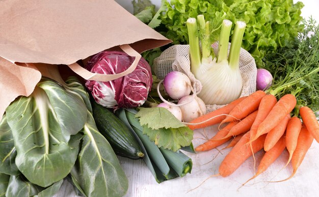 Légumes dans un sac en papier réutilisable parmi d'autres légumes frais sur un tableau blanc