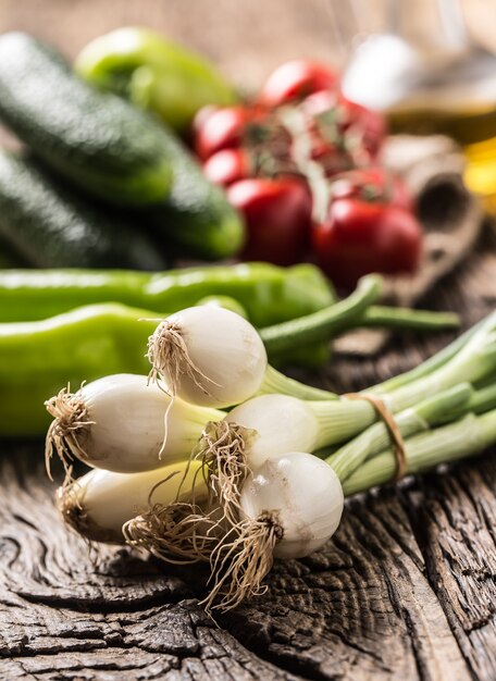 Légumes frais concombre oignon poivron et tomates sur table rustique en chêne.