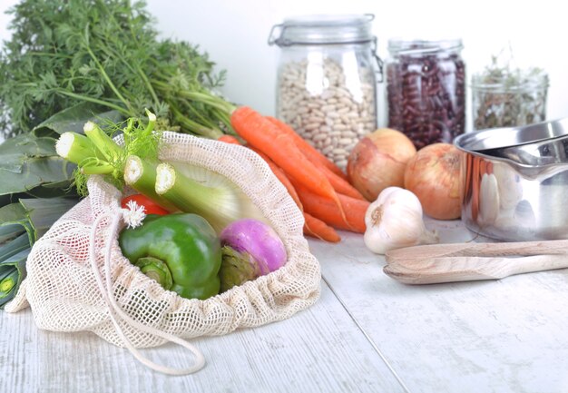 Légumes frais dans un sac réutilisable et haricots secs en pot avec des oignons, de l'ail et une casserole sur une table