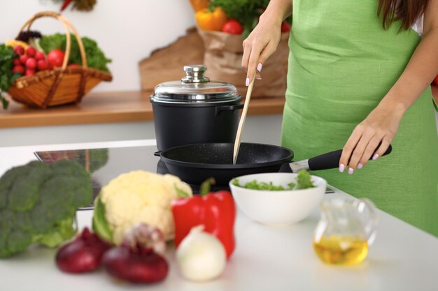 Des légumes frais, de la salade et de l'huile végétale à l'arrière-plan de la femme cuisinent près de la cuisinière dans la cuisine.