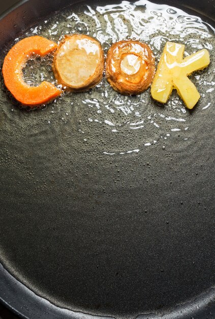 Légumes frits sous forme de lettres sur une poêle à l'huile