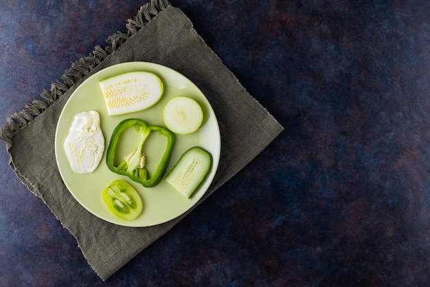 Légumes et fruits frais sur une assiette verte. Divers légumes sur un mur sombre. Poivrons, tomates, concombre, chou, courgettes et pomme pour végétalien. Vue de dessus. Copier l'espace