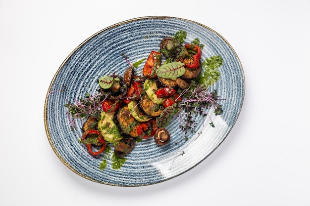 Légumes grillés courgettes, aubergines, champignons, poivrons combinés avec du beurre vert dans une assiette bleue, sur une surface blanche
