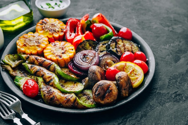 Légumes grillés dans un bol sur fond de pierre sombre Courgettes Poivrons Maïs doux Tomates Oignons rouges et aubergines