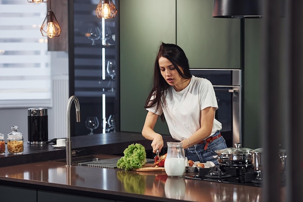 Légumes et lait sur la table Préparation des aliments Jeune belle brune en vêtements décontractés à l'intérieur dans la cuisine pendant la journée