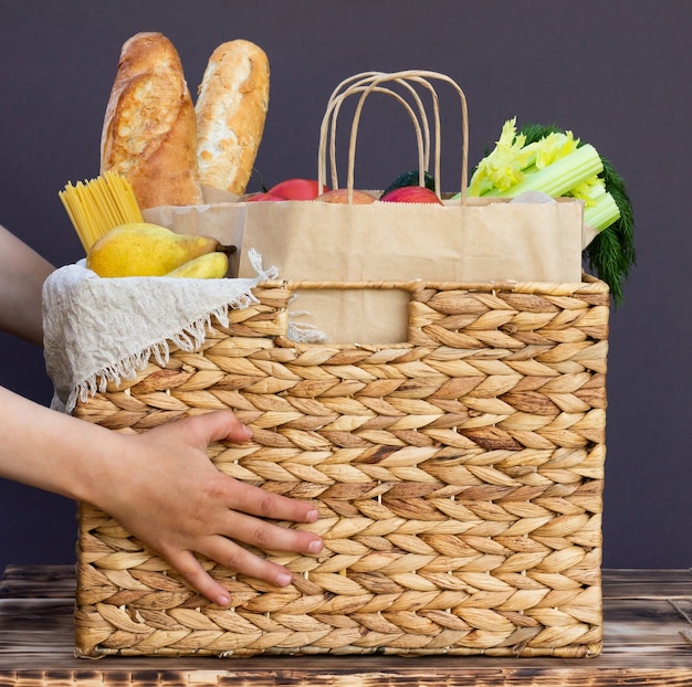 Légumes, légumes verts et fruits bio écologiques frais, céréales et pâtes dans un panier en osier entre les mains d'un enfant. Livraison ou don de concept alimentaire agricole écologique