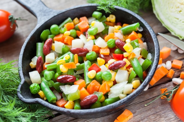 Légumes mélangés dans une poêle à frire rétro et ingrédients sur une table rustique en bois