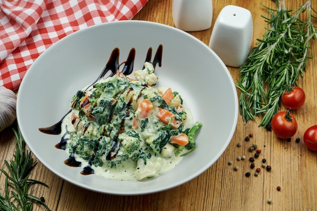 Légumes mijotés (carottes, brocolis et épinards) en sauce à la crème avec du fromage dorblu dans une fiole blanche sur bois.