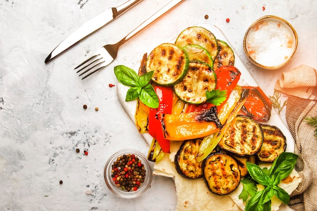 Légumes multicolores grillés aubergines courgettes poivre au basilic vert sur planche de pierre servant sur fond gris vue de dessus