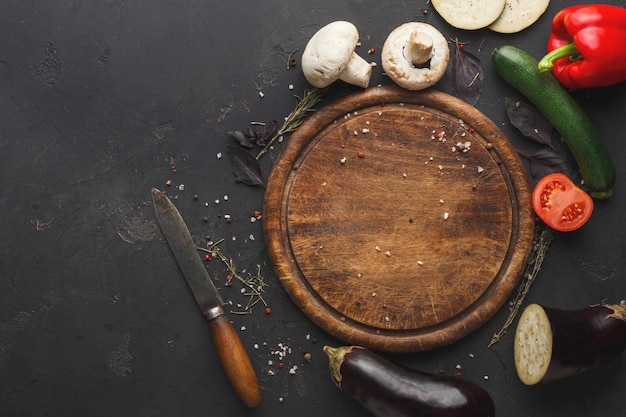 Légumes sur une planche en bois et un couteau sur fond sombre vue de dessus avec espace de copie