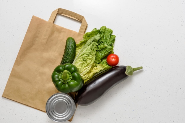 Des légumes, des poivrons rouges et verts, des aubergines, du concombre, des aliments en conserve, de la laitue et un gant en caoutchouc reposent sur un sac en papier. Espace de copie vue de dessus. Don. livraison de nourriture sans contact.