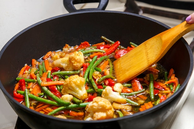 Les légumes en sauce pan-asiatique sont mélangés à la spatule en bois dans une poêle