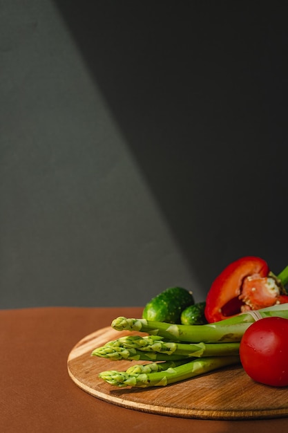 Légumes se trouvent sur une planche de bois tomates asperges concombres poivrons rouges brun fond gris foncé place pour le texte