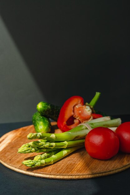 Légumes se trouvent sur une planche de bois tomates asperges concombres poivrons rouges brun fond gris foncé place pour le texte