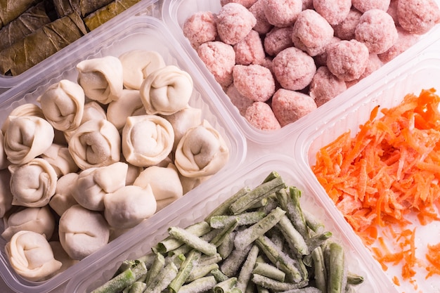 Légumes surgelés et produits carnés semi-finis dans des contenants en plastique sur une plaque blanche. boulettes de viande, boulettes, haricots hachés et carottes râpées