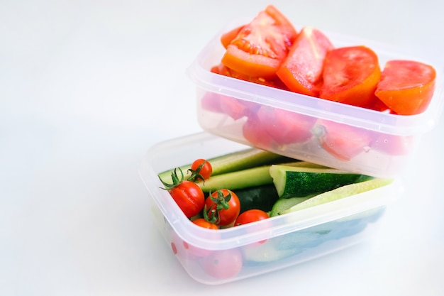 Légumes tranchés dans des récipients en plastique sur fond blanc. Les concombres et les tomates sont dans des conteneurs.