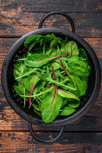 Légumes verts frais crus, épinards, bette à carde et roquette. Fond en bois foncé. Vue de dessus.