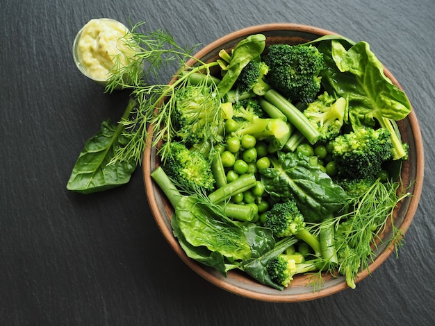 Légumes verts frais dans une assiette en bois sur une surface sombre