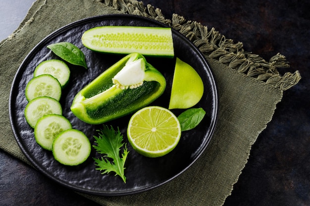 Légumes verts et fruits sur fond sombre. Alimentation diététique sur une serviette en lin. Nourriture végétarienne saine sur une plaque noire. Vue de dessus