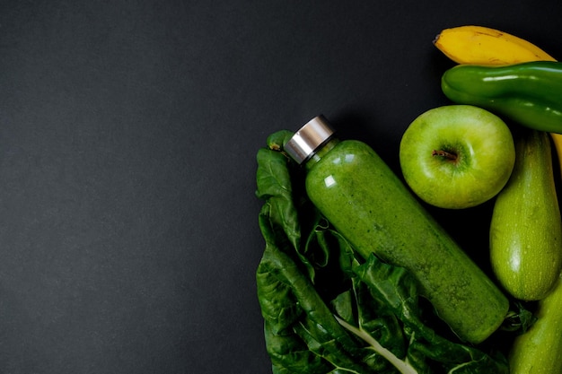 Légumes verts et smoothies dans une bouteille en plastique sur fond noir Concept sain Vue de dessus Espace pour le texte