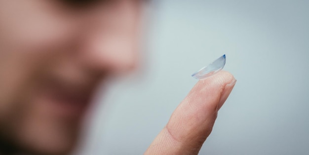 Lentille de contact allongée sur une macro de doigt mâle en gros plan Patient client ou œil dans l'arrière-plan flou