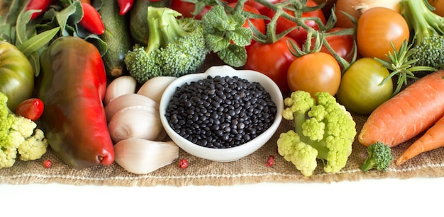 Lentilles noires non cuites dans un bol avec des légumes isolated on white close up