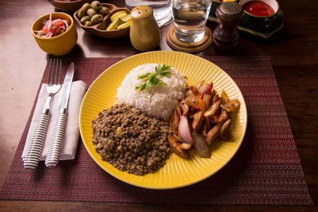 Lentilles poulet sauté riz cuisine traditionnelle péruvienne mise en place table en bois