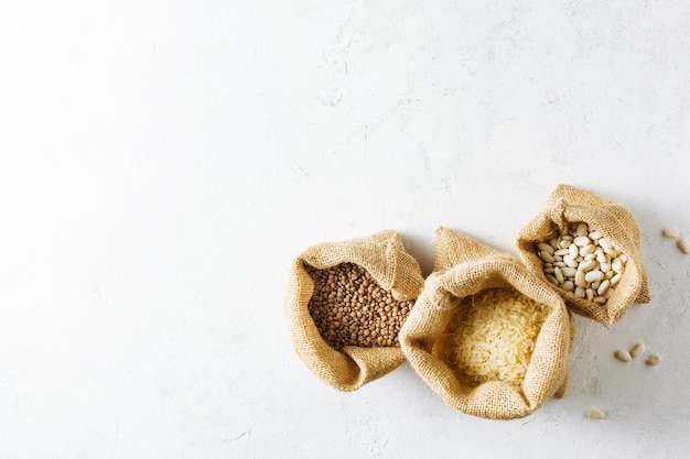 Lentilles de riz et haricots blancs dans des sacs en toile sur fond clair avec une copie de l'espace