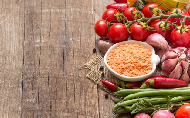 Lentilles rouges sèches crues dans un bol et légumes sur une table en bois se bouchent avec copie espace