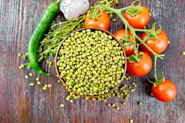 Photo lentilles vertes mung dans un bol, piments forts, ail, thym et tomates rouges sur fond de planche de bois d'en haut