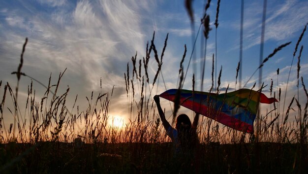 Une lesbienne bisexuelle transgenre tient le drapeau LGBT sur fond de ciel au coucher du soleil et célèbre un défilé gay Journée de la bisexualité ou Journée nationale du coming out pendant le mois de la fierté