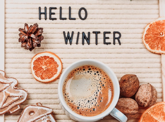 Lettrage bonjour l'hiver sur le tableau des lettres branches de sapin séchées oranges noix et une tasse de café fond de nouvel an minimaliste 2023