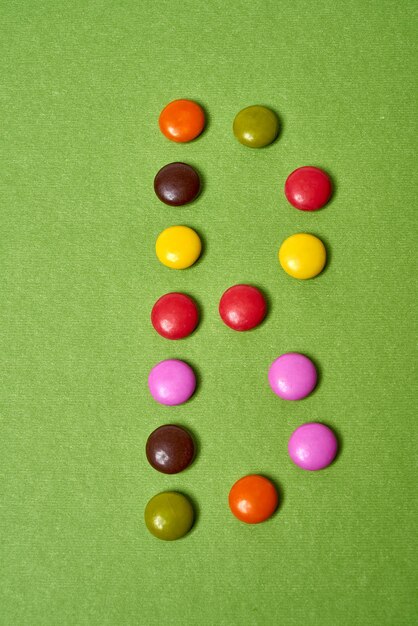 Lettre B écrite avec des bonbons au chocolat ronds colorés sur fond vert.