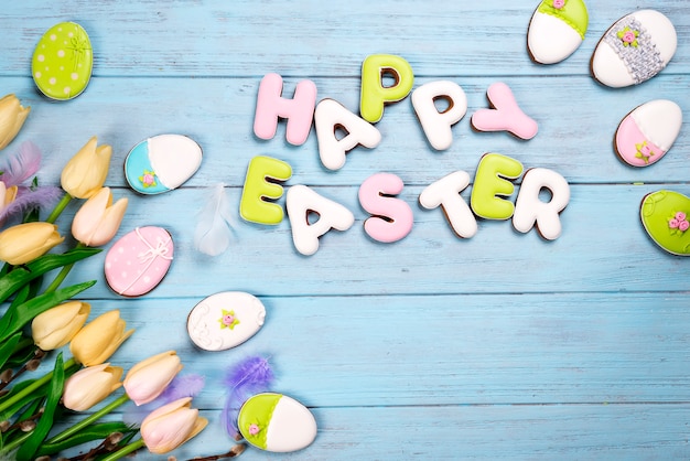 Lettre de biscuits de Pâques Joyeuses Pâques et oeufs colorés avec des tulipes sur fond de bois