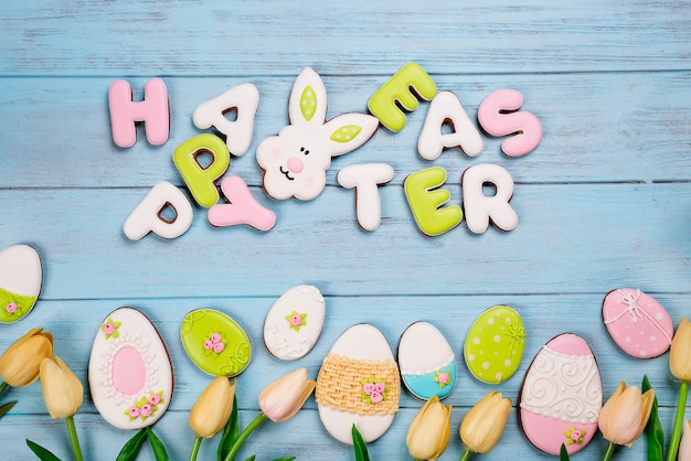 Photo lettre de biscuits de pâques joyeuses pâques et oeufs colorés avec des tulipes sur fond de bois