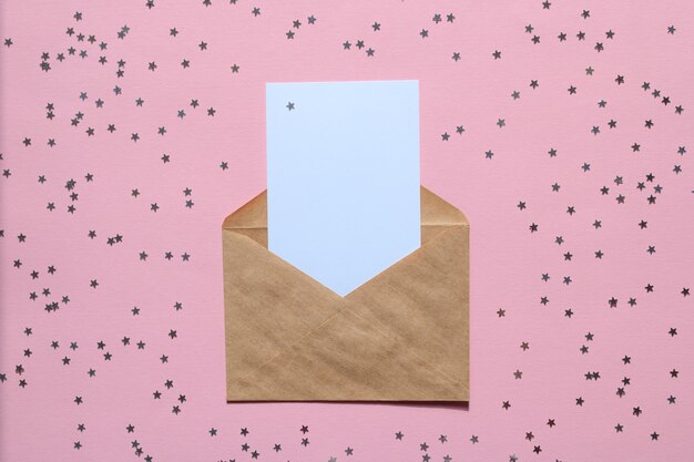 Lettre enveloppe en papier kraft avec maquette de carte blanche vierge sur fond rose avec des étoiles de confettis.