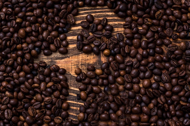 Lettre F de grains de café. Grains de café torréfiés sur fond de bois