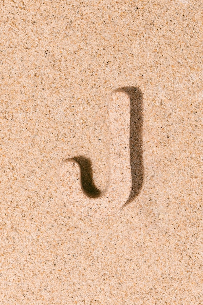 Photo lettre j du sable isolé sur le concept de sable de plage de l'alphabet d'été