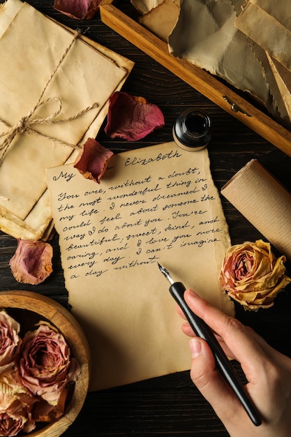 Photo lettre avec texte pétales de rose et stylo à encre à la main sur la vue de dessus de fond en bois