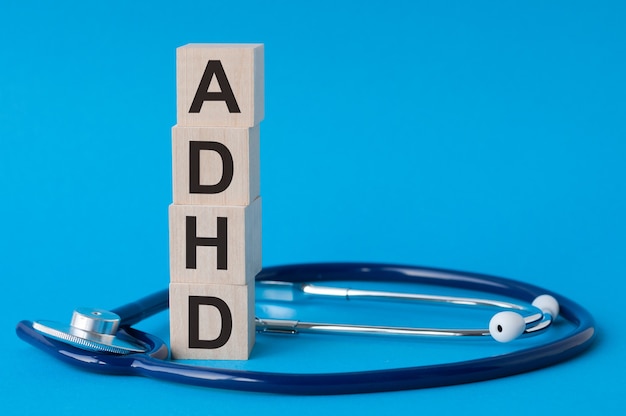 Lettres ADhd écrites sur des blocs de bois et stéthoscope sur une surface bleu clair