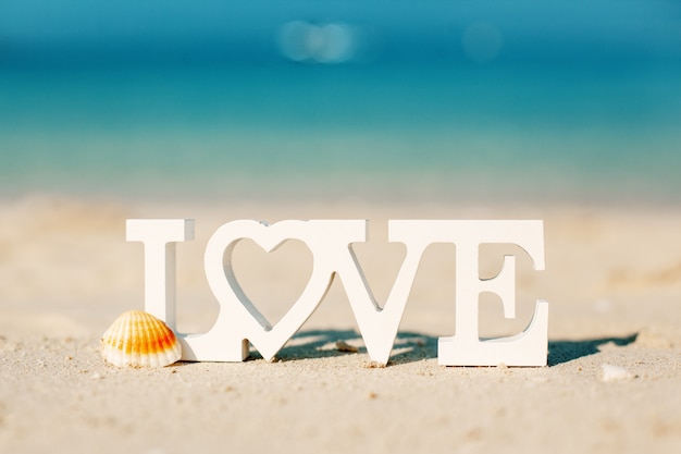Photo lettres en bois amour sur une plage de sable surplombant la mer bleue
