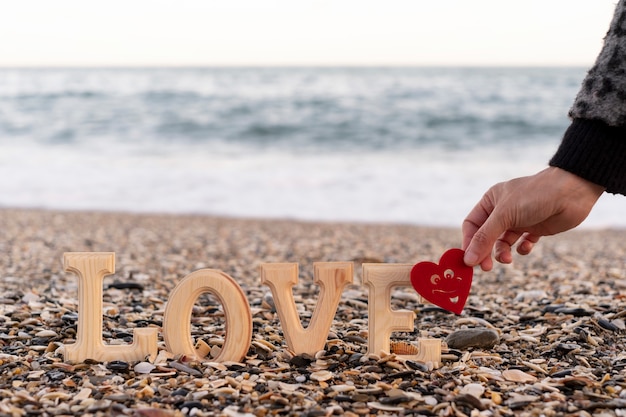 Lettres En Bois Formant Le Mot Amour Et Une Main Tenant Un Coeur Rouge Au Bord De La Mer. Concept De St. La Saint-valentin