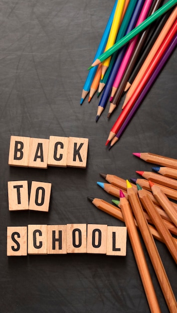 Lettres carrées en bois avec la phrase "Retour à l'école" écrite en anglais sur un fond de tableau noir et à côté de crayons de couleur