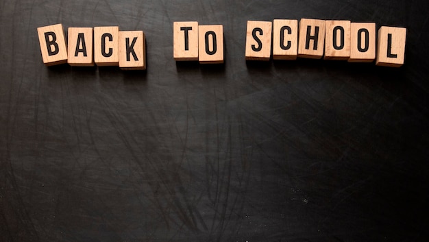 Lettres carrées en bois avec la phrase "Retour à l'école" écrite en anglais sur un fond de tableau noir