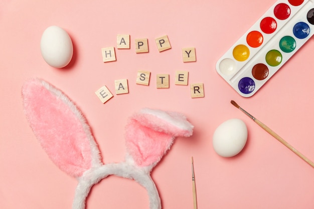 Lettres avec des œufs, des peintures colorées et des oreilles de lapin isolés sur fond rose