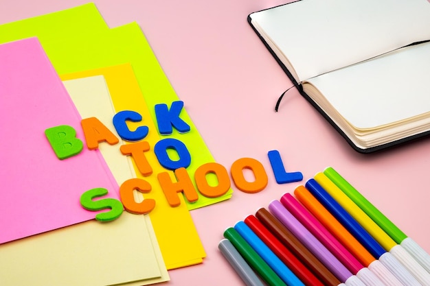 Lettres de retour à l'école, avec des fournitures scolaires sur une table rose.